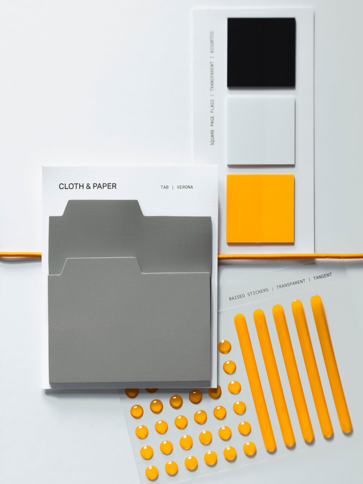Gray folder-shaped Tab Sticky Notes, transparent Square Page Flags in black, white and orange, and orange Raised Stickers in dots and bars, laid out on a white surface.