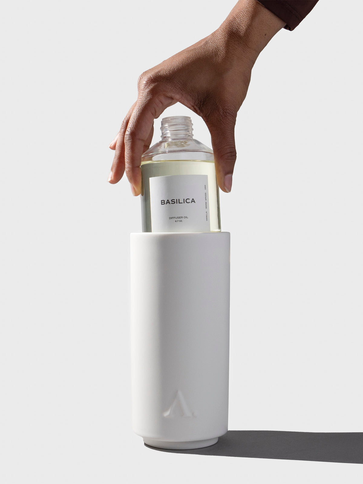 A hand is shown lifting a bottle of Basilica oil out of the diffuser vessel.