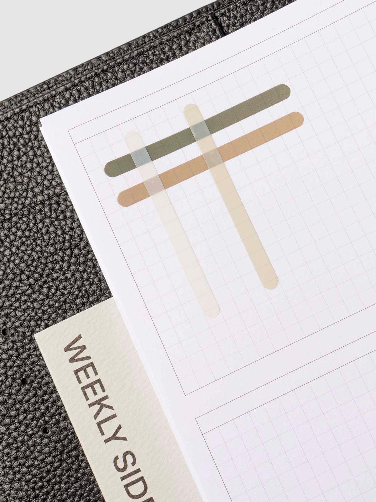 Set of four sticker sheets layered over each other on an insert inside a black leather planner. 