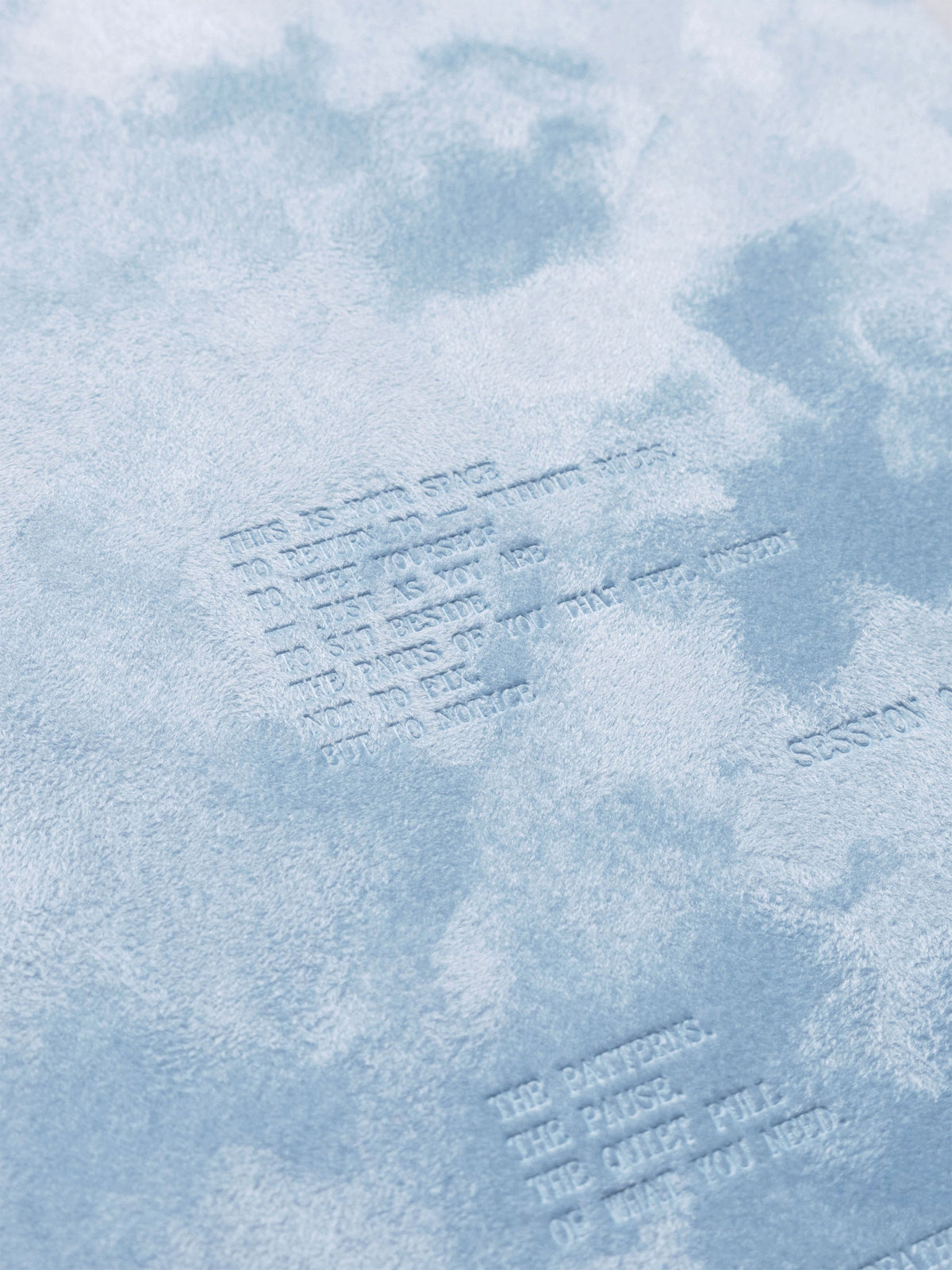 A close up of the debossed text design and velvet texture on the blue Break Room spiral notebook.