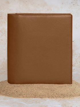 Folio displayed on a textured tan background, placed in a pile of sand. Color pictured is clay brown. 