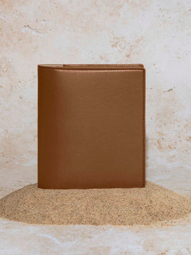 Folio displayed on a textured tan background, placed in a pile of sand. Color pictured is clay brown.