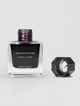 The Avant Garde ink bottle shown open, with the black cap set beside it, revealing a deep ink inside.