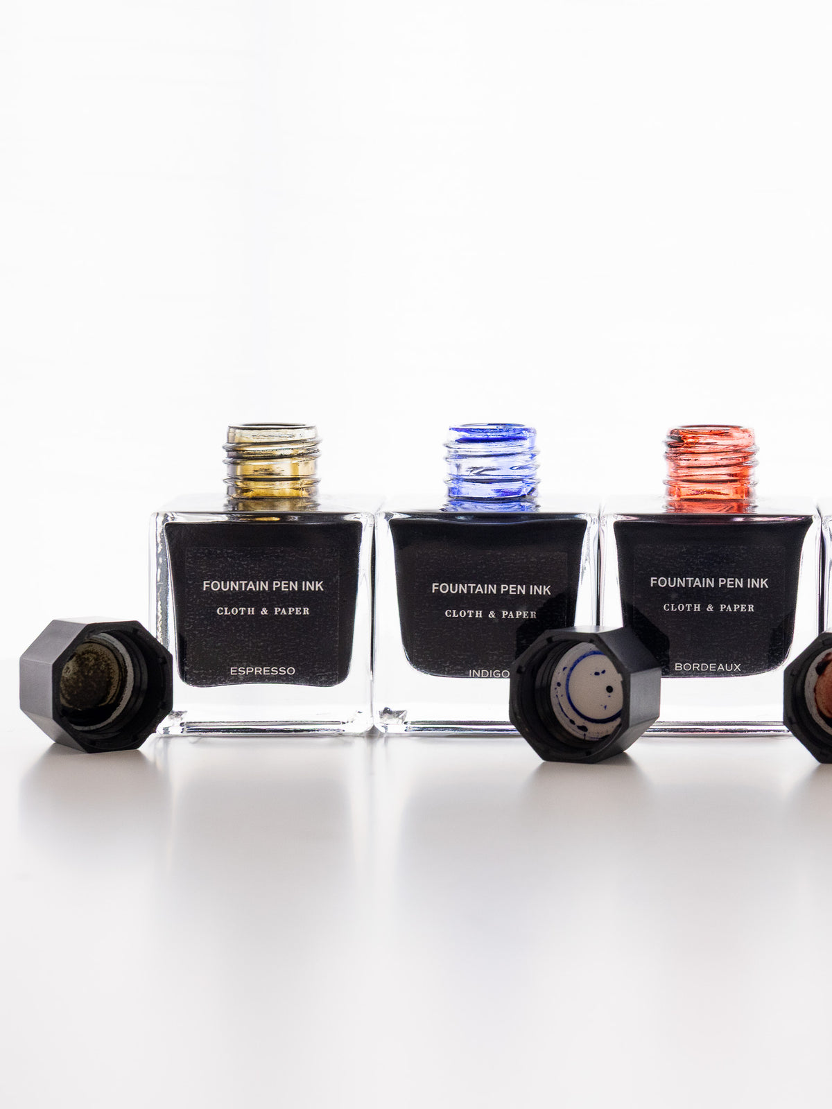 Cloth & Paper fountain pen ink bottles in Espresso, Indigo, and Bordeaux colors with caps removed, showing ink-stained bottle openings.
