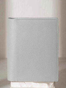 Heirloom Leather Folio, Small, Cloth and Paper. Veleta folio displayed on a white stone pedestal. The background is a natural textured off-white material, and a spotlight behind the folio highlights its placement.
