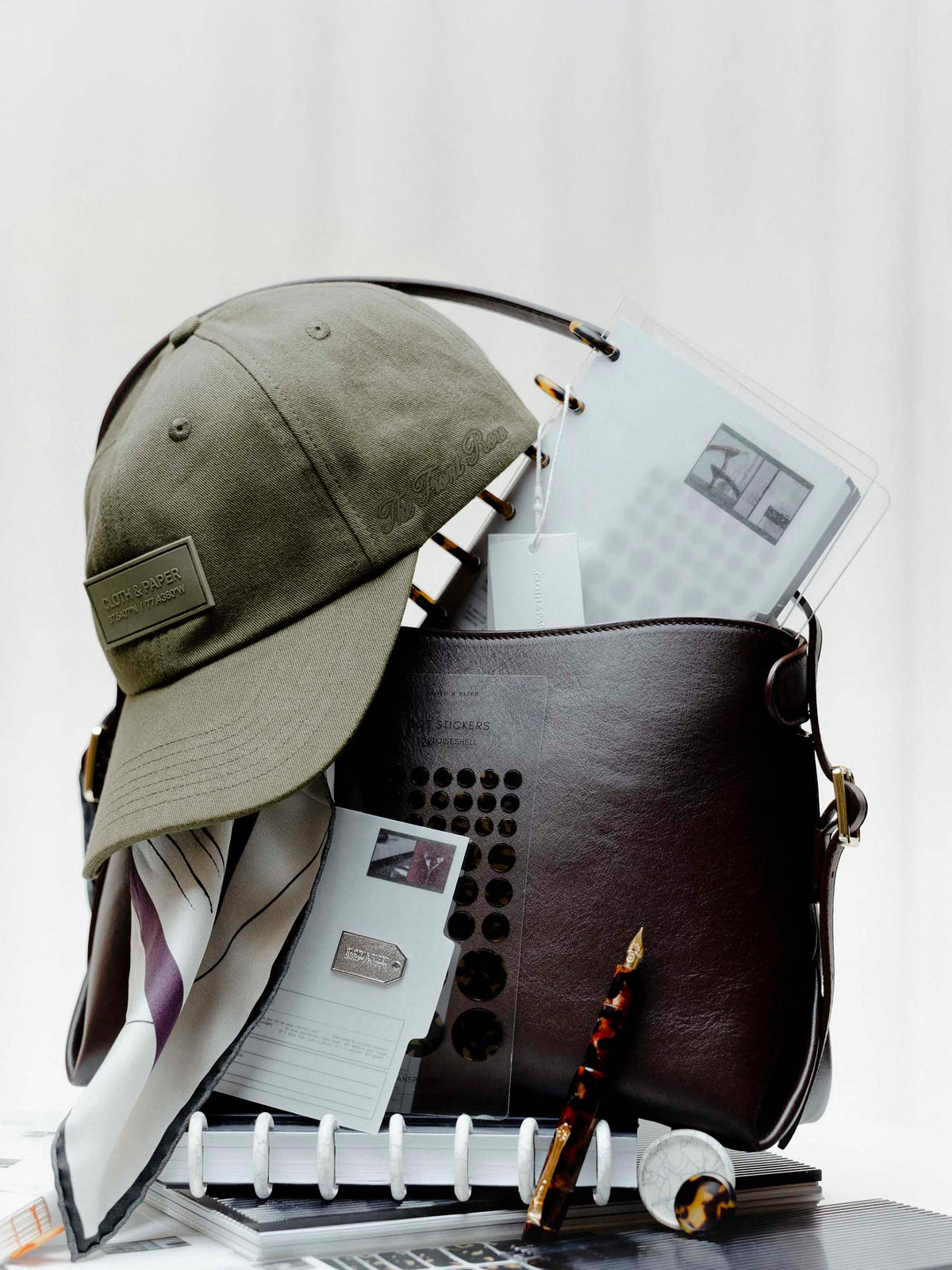 Several Planner Essentials and accessories from the Front Row Collections staged inside a Valencia Bag.  Heavily featured are the Label Hat, Planner Brooch | Tag, and Kaweco Art Sport Fountain Pen in Hickory Brown.