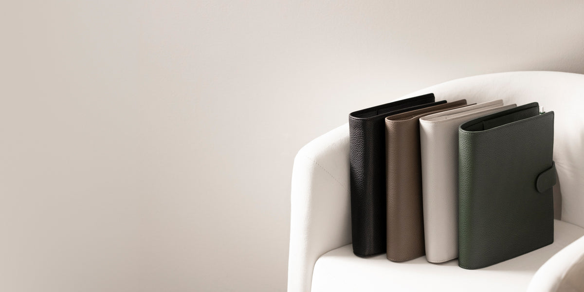 Several Foundations 6-Ring Leather Agendas in a variety of colors are sitting on a white chair.