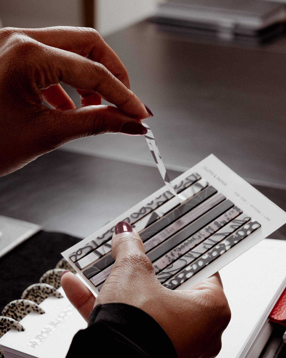 Hands peeling a single patterned Page Pin | Long from a Cloth & Paper sheet with a planner in the background