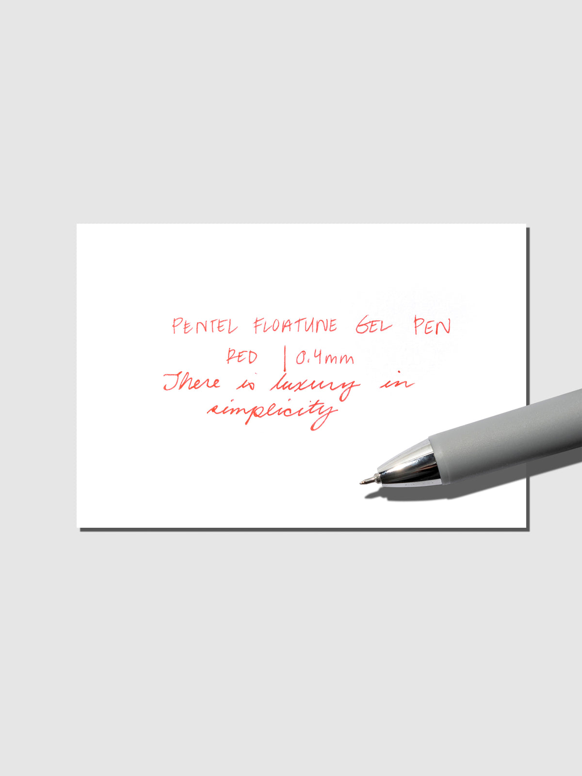 Pentel Floatune Gel Pen 0.4mm red ink. Pen resting on pen test sheet displaying writing sample.