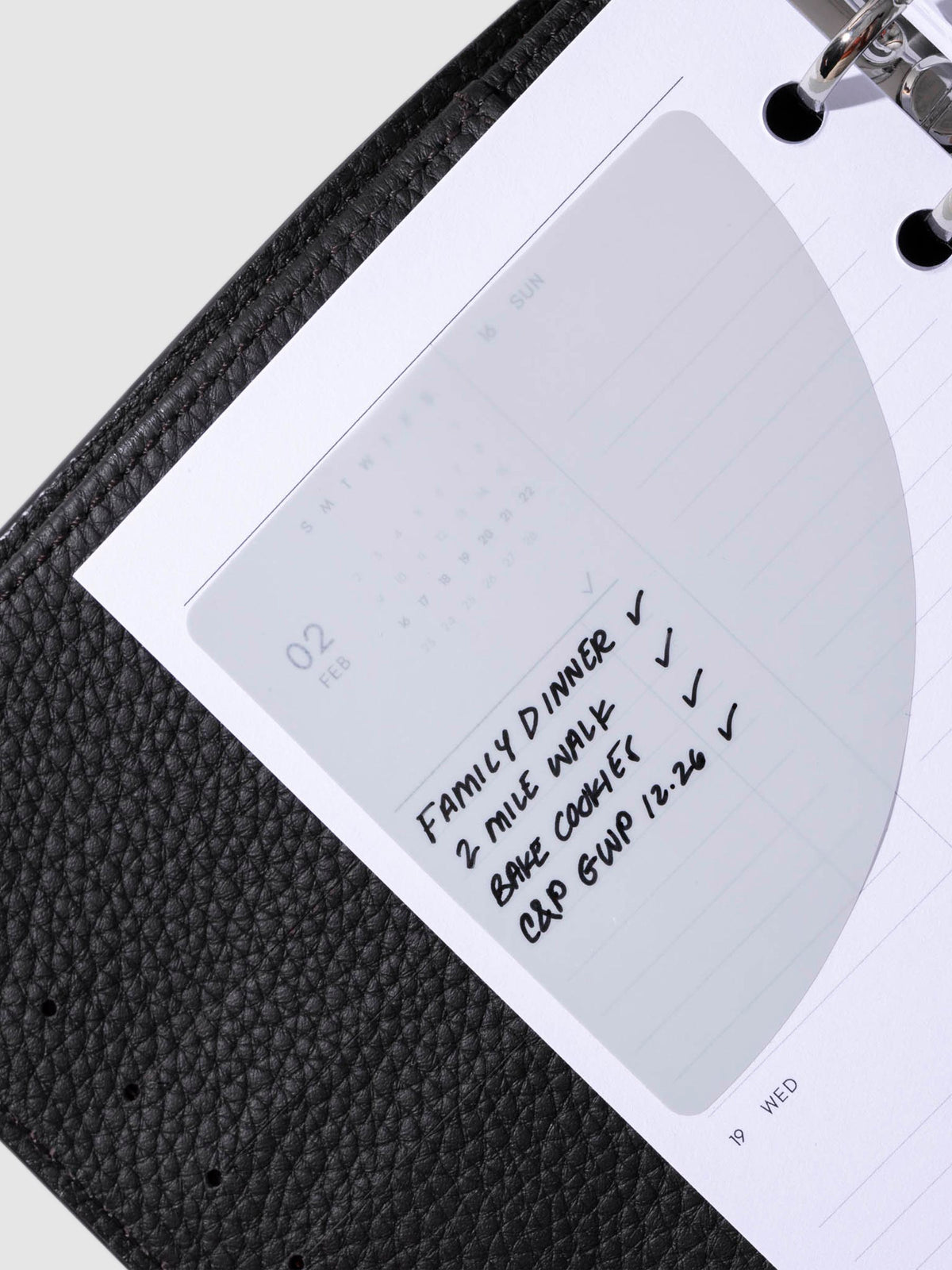 Sticky note in use inside a black leather planner. It is written on with a black oil based ink pen.