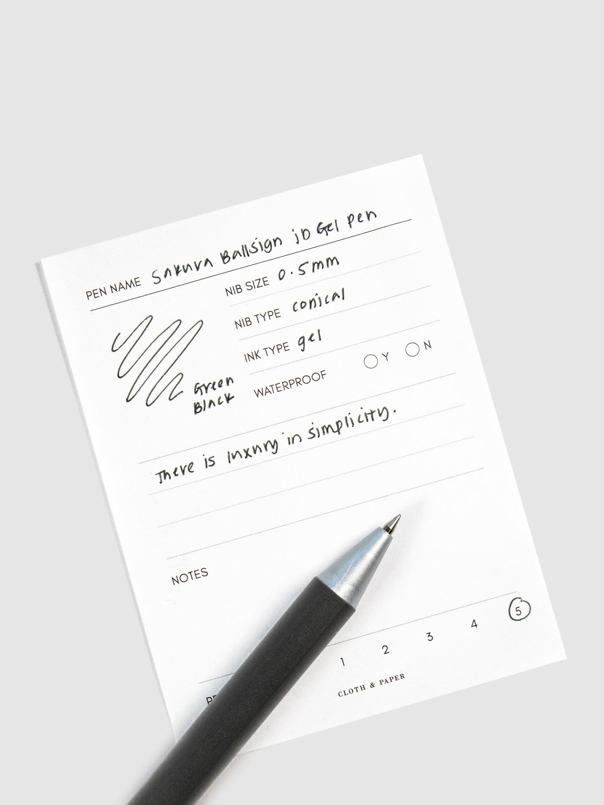 Pen in Green Black resting on a pen test sheet displaying a writing sample detailing the pen's specs.