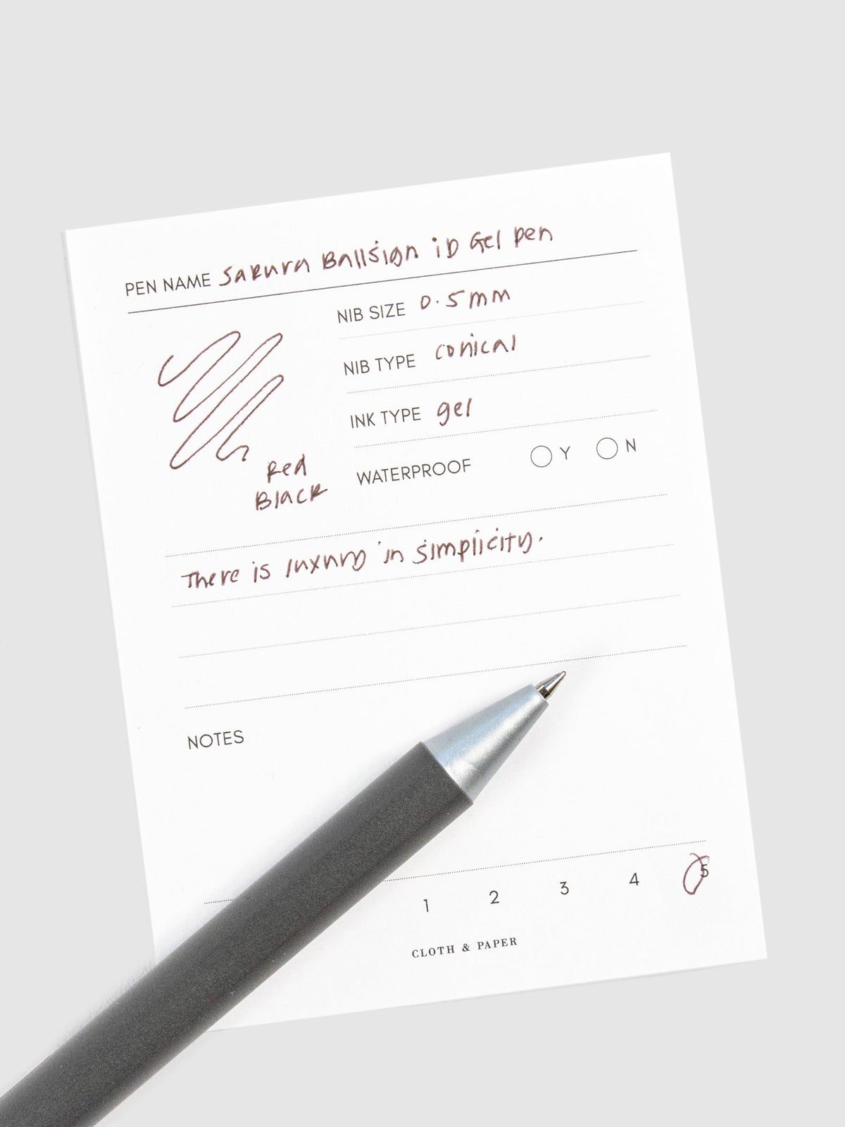 Pen in Red Black resting on a pen test sheet displaying a writing sample detailing the pen's specs.