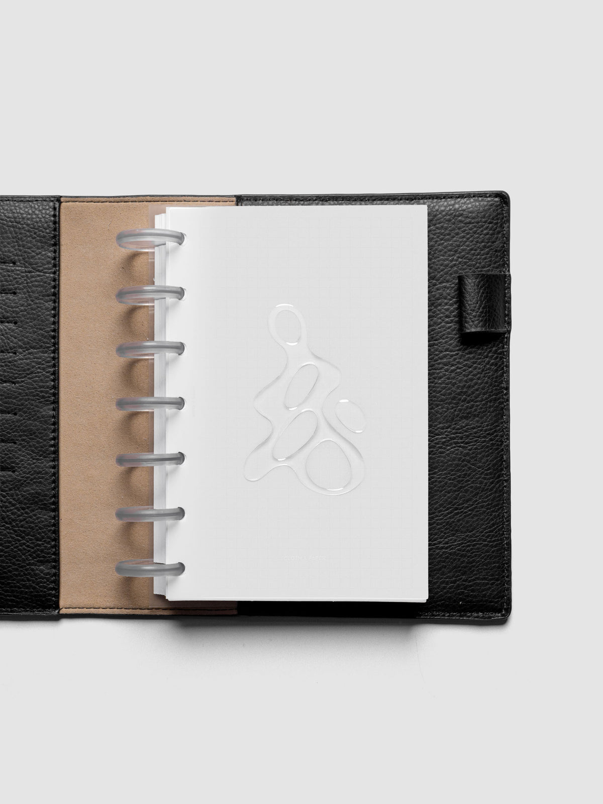 Light grey, semi-transparent, and glossy plastic planner dashboard with organic raised shape design in size HP Mini shown discbound in a black leather folio.