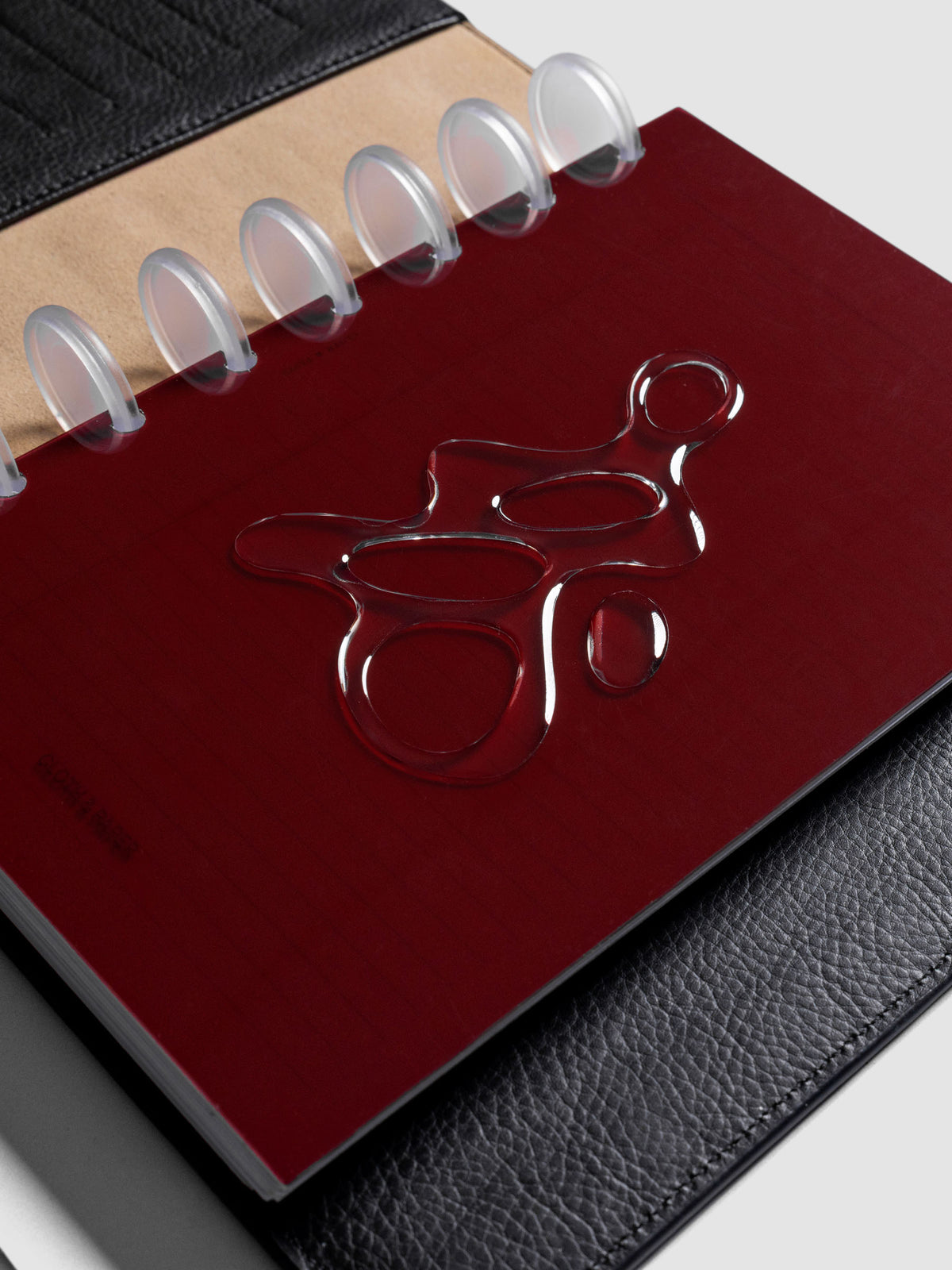 Dark red, semi-transparent, and glossy plastic planner dashboard with organic raised shape design in size Half Letter shown discbound in a black leather folio.