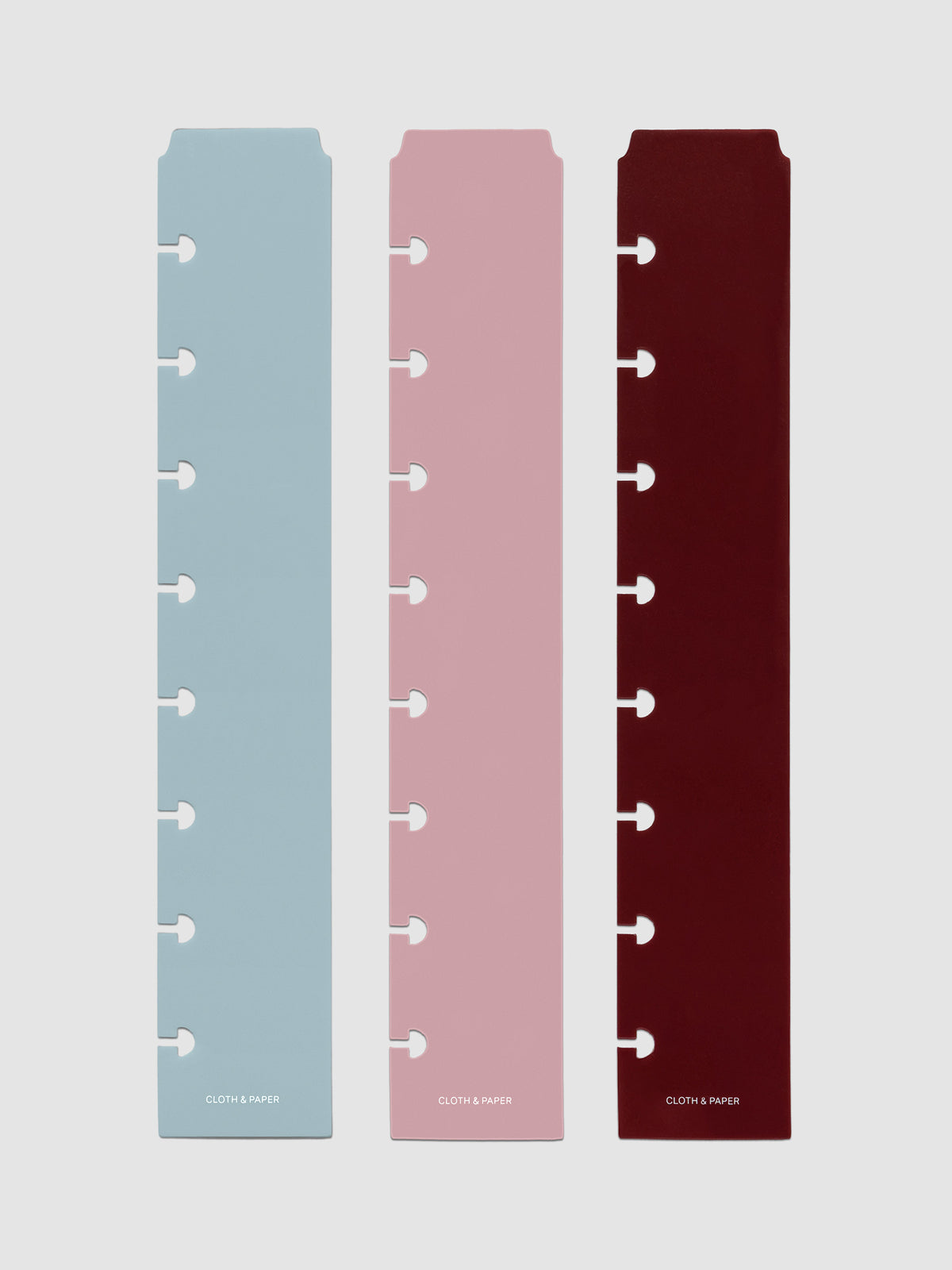 Set of three narrow page markers pre-punched for Half Letter planners in light blue, pink, and burgundy on a neutral background.