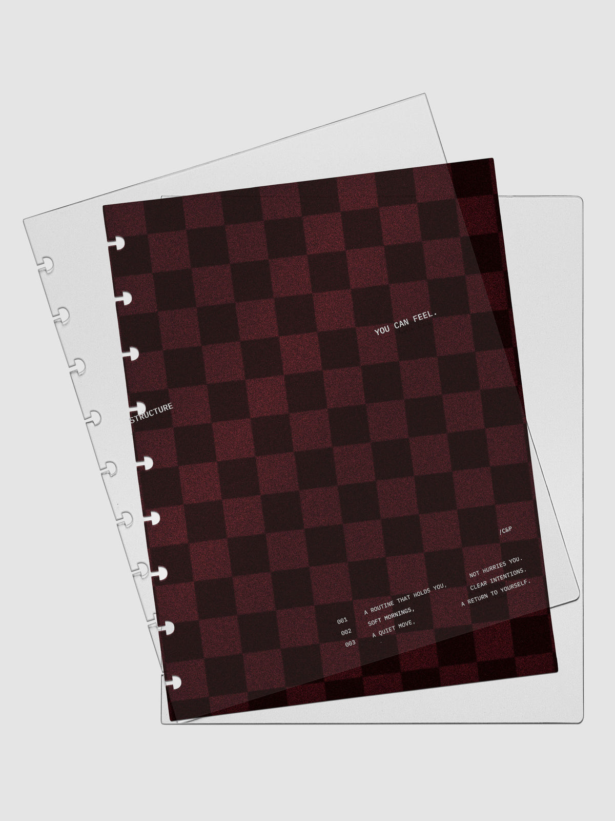 HP Classic sized velvet checkered dashboard in the color Bordeaux in between two crystal clear plastic planner covers with text printed on the cover on the theme of structure and routines.