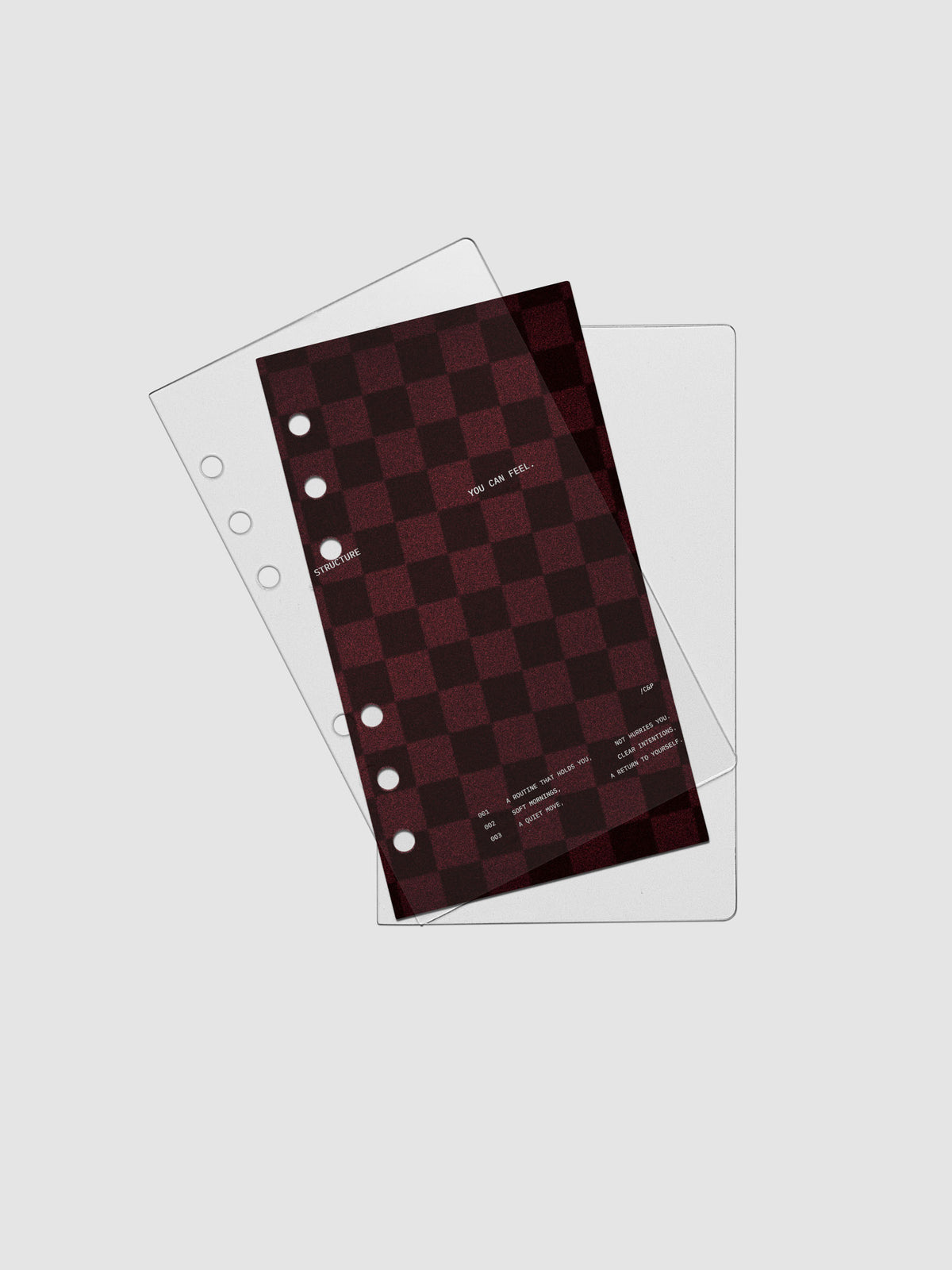 Personal sized velvet checkered dashboard in the color Bordeaux in between two crystal clear plastic planner covers with text printed on the cover on the theme of structure and routines.