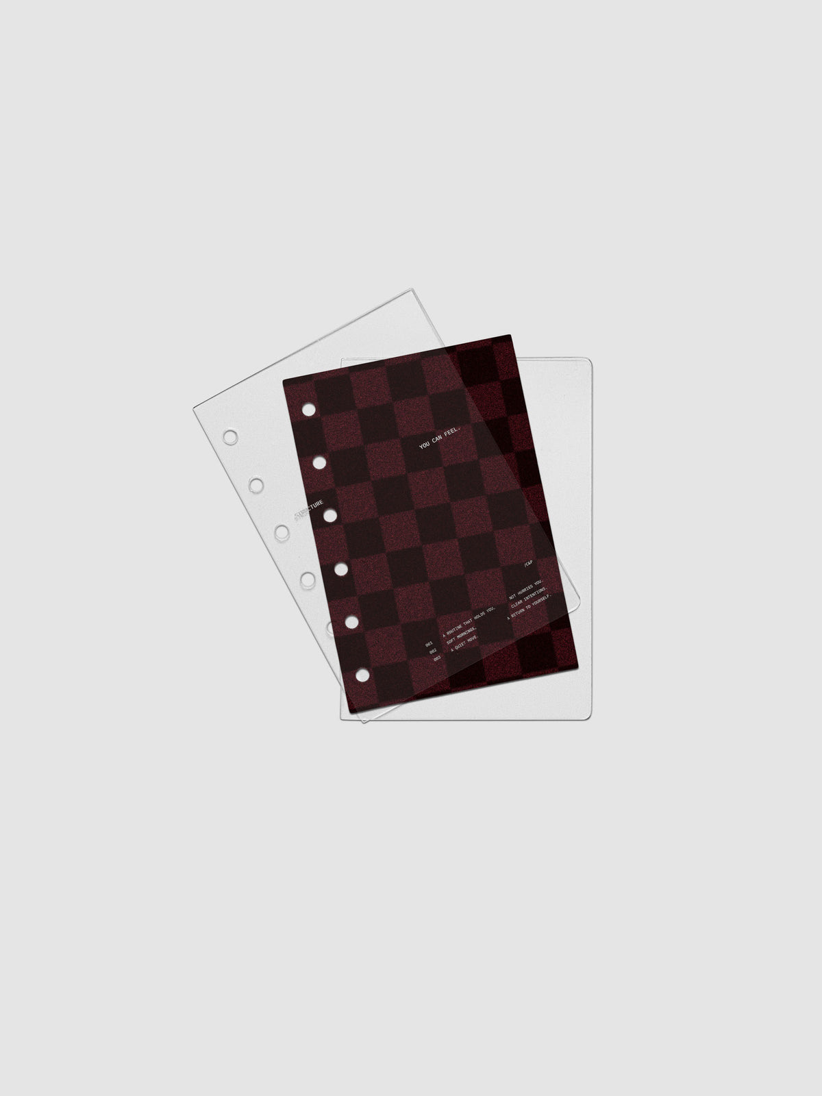 Pocket sized velvet checkered dashboard in the color Bordeaux in between two crystal clear plastic planner covers with text printed on the cover on the theme of structure and routines.
