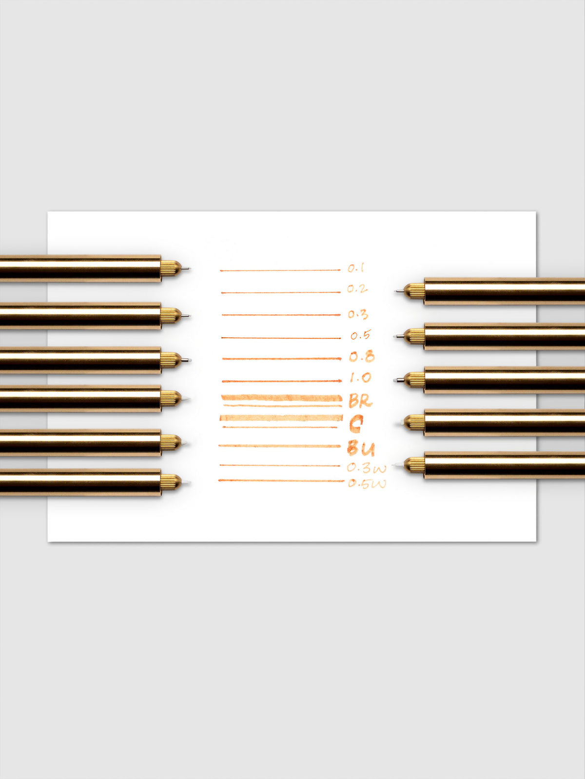 Collection of Lumos Pro Pens in a brass finish showing writing samples on paper with each nib size.