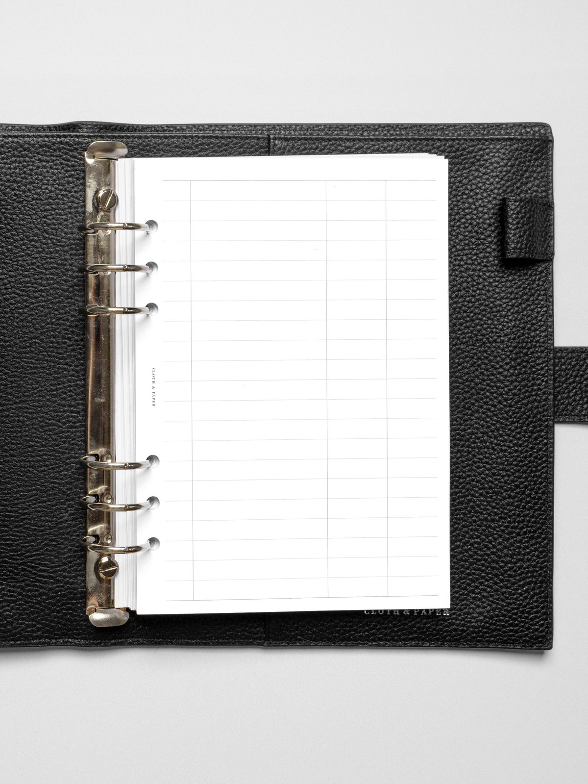A5-sized Tracker Planner Insert displayed in a black leather ring-bound planner, featuring a clean grid layout with lined sections.