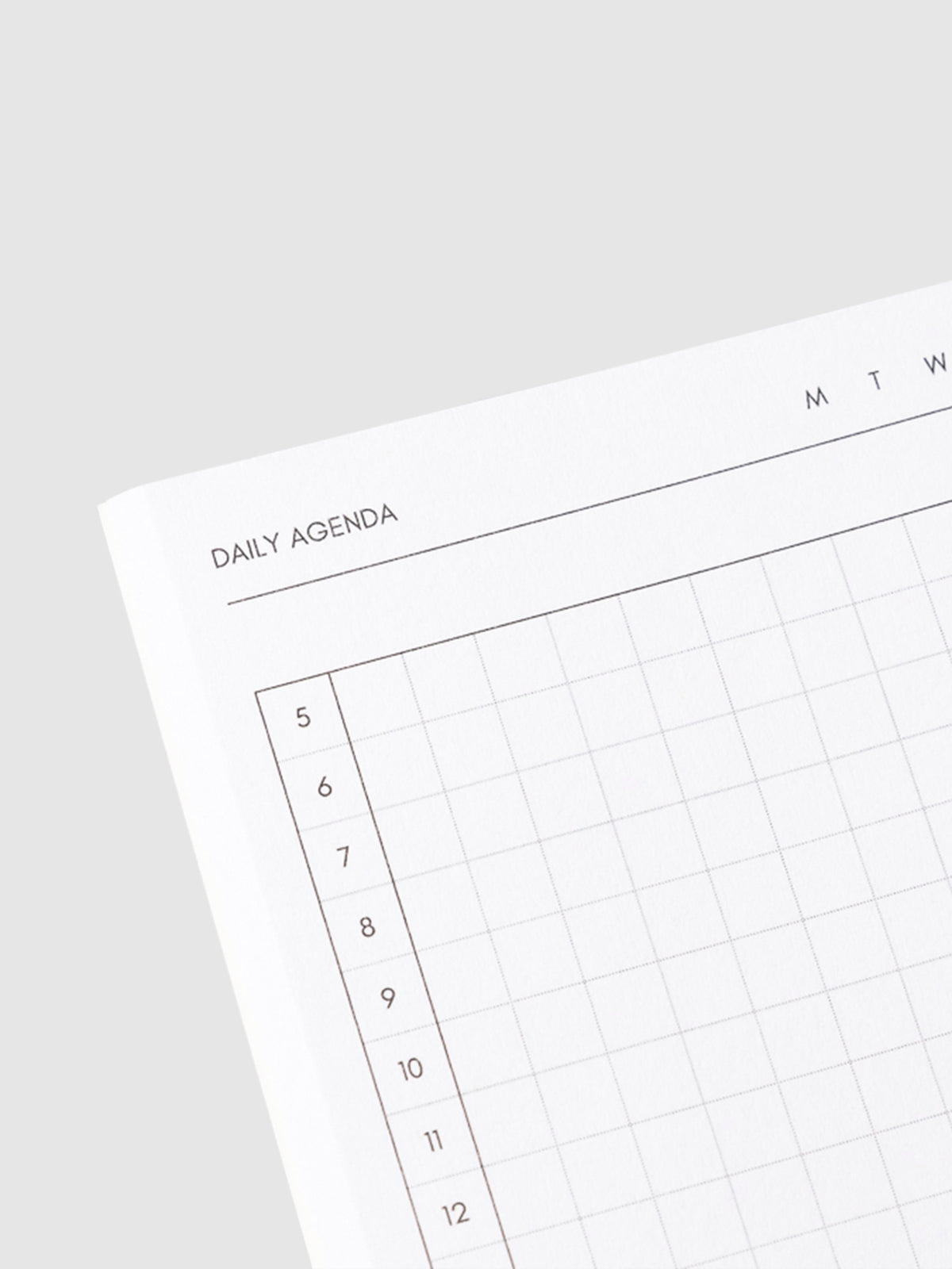Close up image of the top left corner of the daily agenda notebook page. The page is turned on a left angle and is displayed on a light gray background