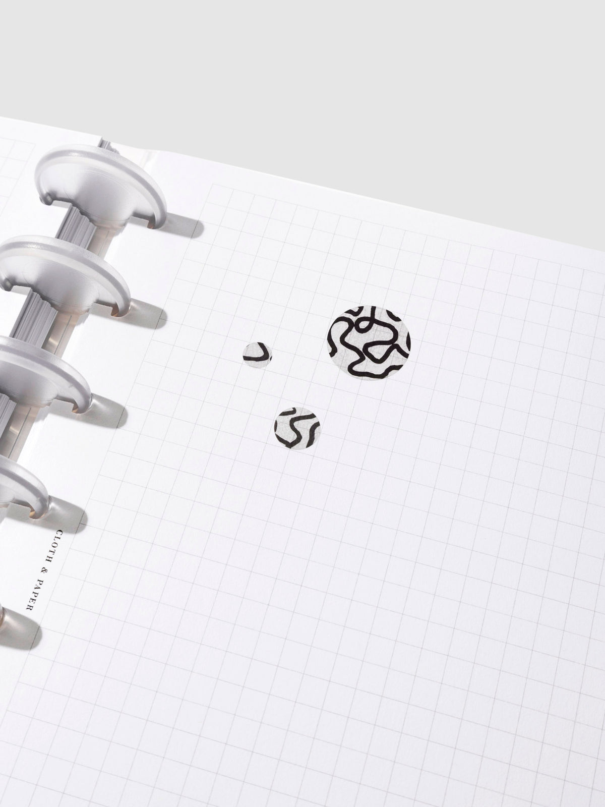A small, medium, and large sticker are pressed onto a page in a discbound planner.