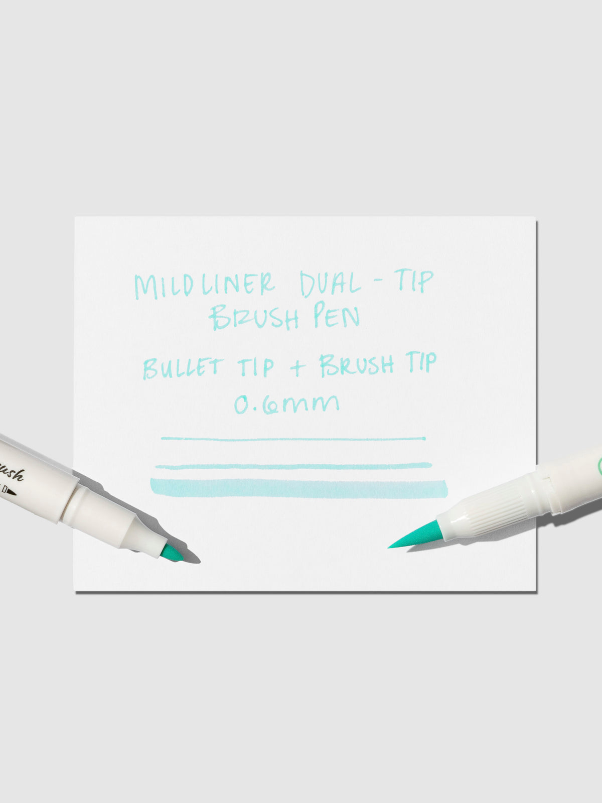 Brush pen tip resting on Blue Green pen test sheet displaying writing sample that details pen specs.