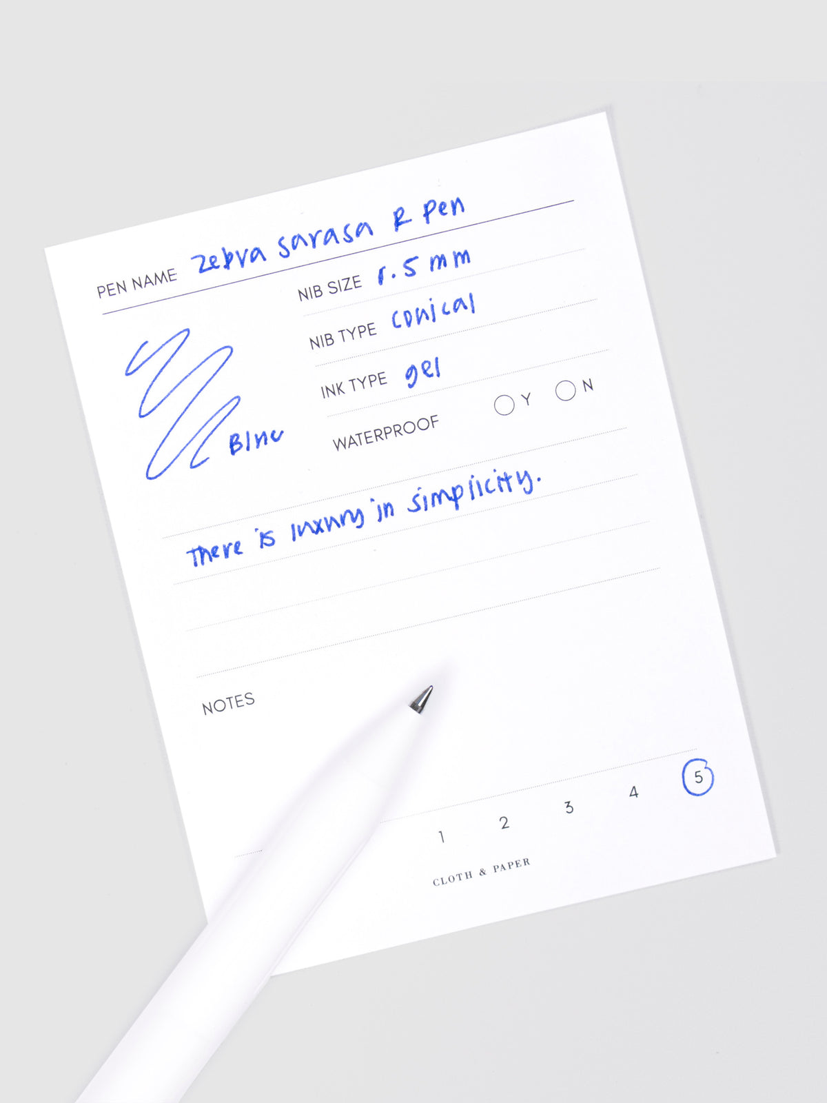 Zebra Sarasa R Pen, 0.5 mm, Blue, Cloth and Paper. Pen resting on pen test sheet displaying writing sample.